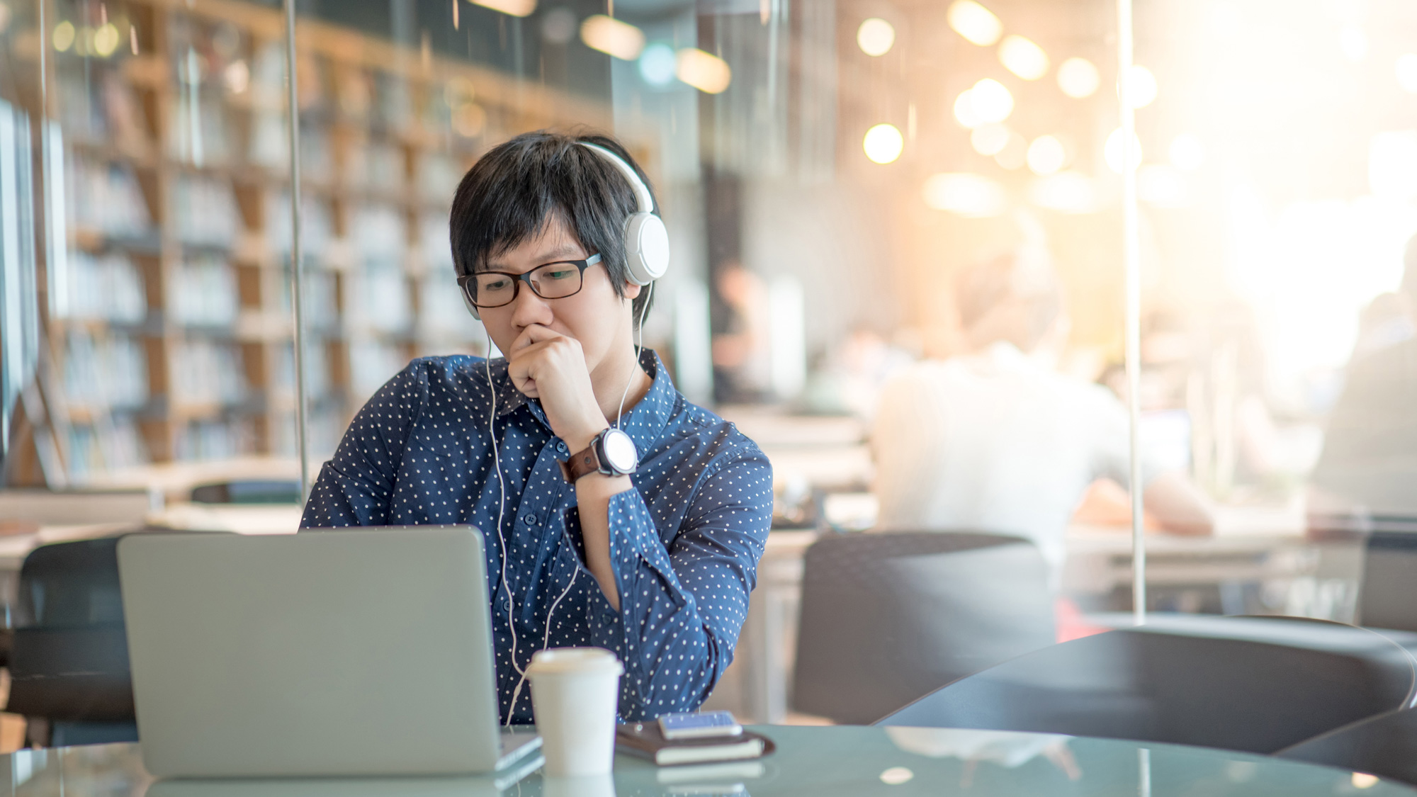 A man sitting at a laptop with headphones on, reading.