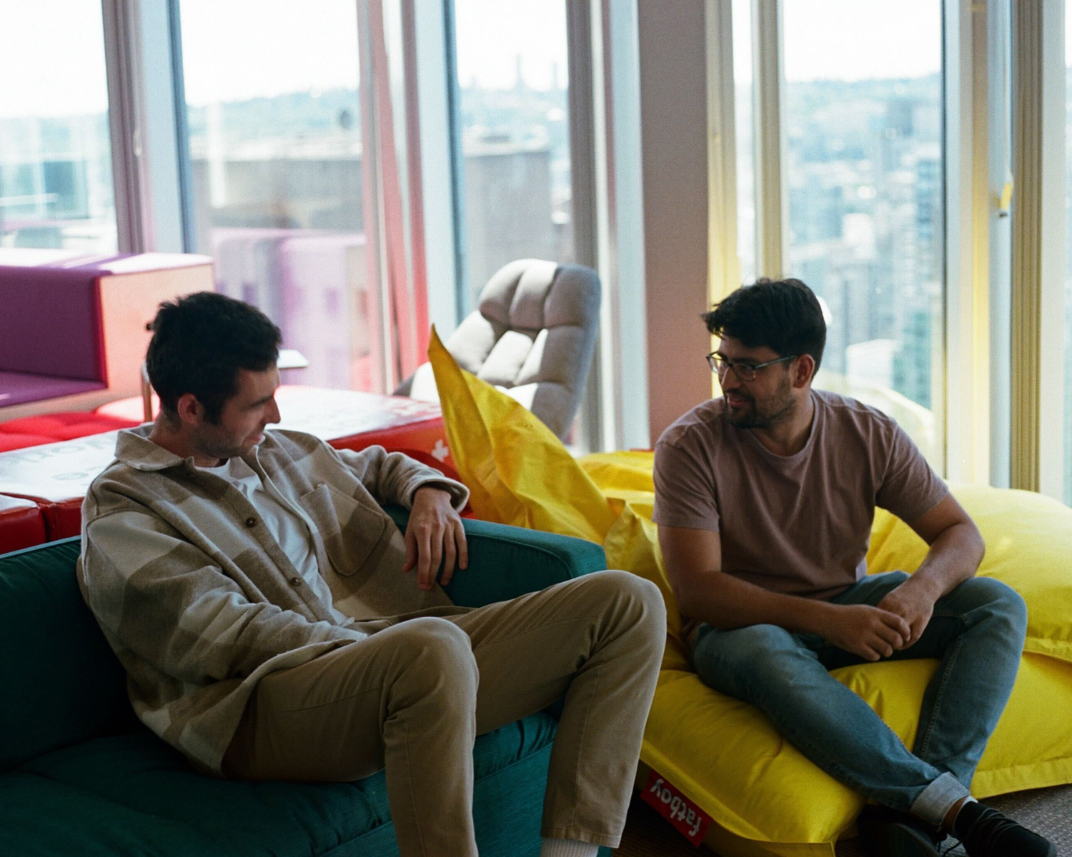 Two men sitting in bean bag chairs talking and smiling.